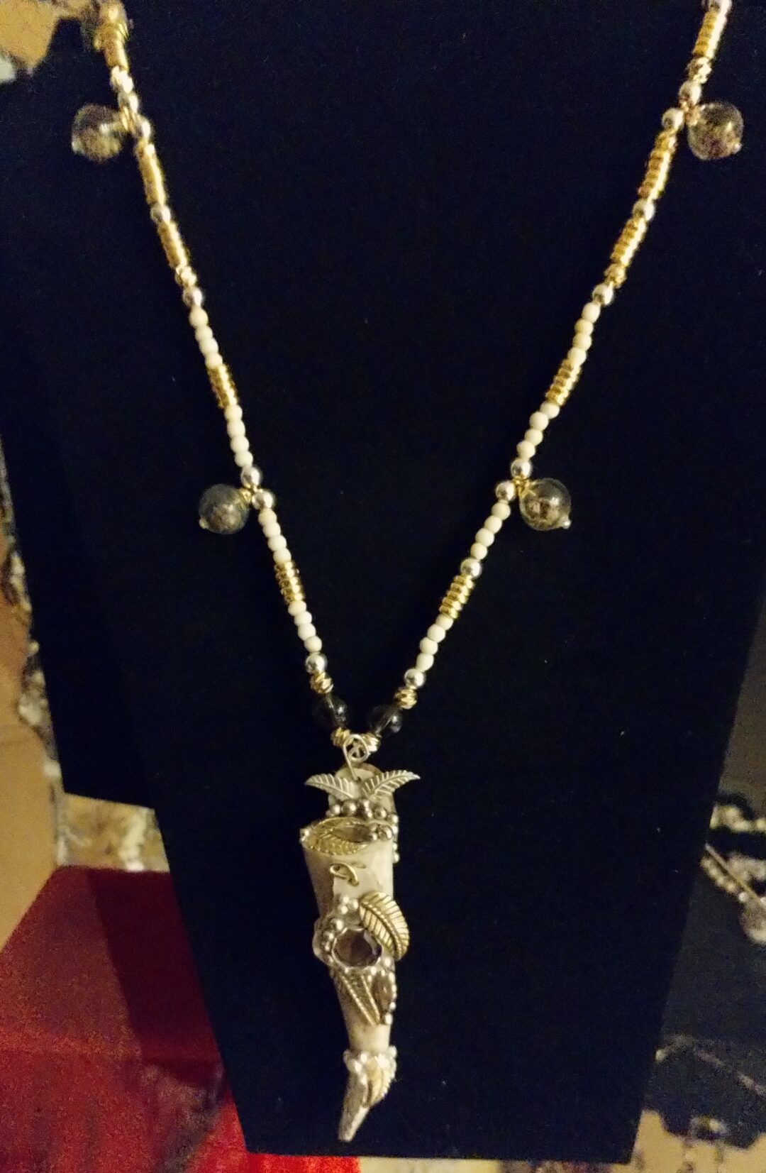 Beaded necklace with a pendant and small charms against a dark background.