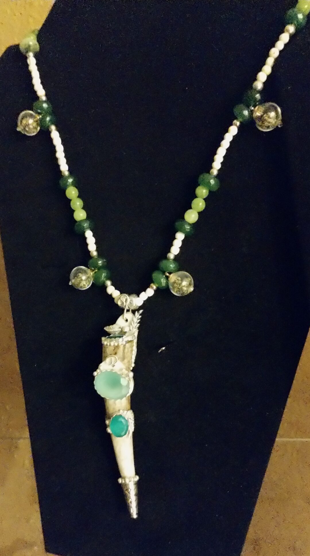 Handmade necklace with green beads and a pendant on a black background.