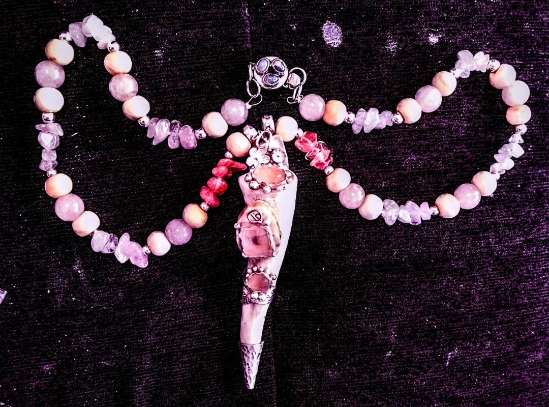 Delicate pink beaded necklace with a floral pendant on dark background.