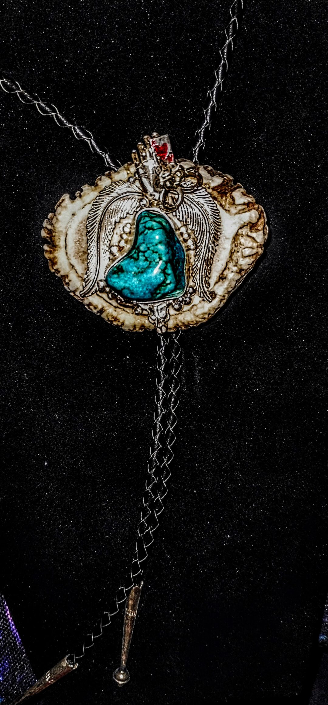 Close-up of a turquoise stone pendant with intricate wire wrapping on black background.