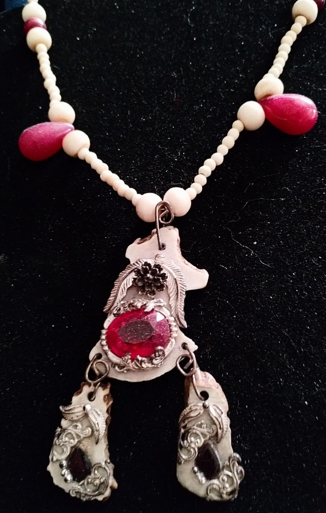 Intricate pendant with red stones and dangling charms on a braided necklace.